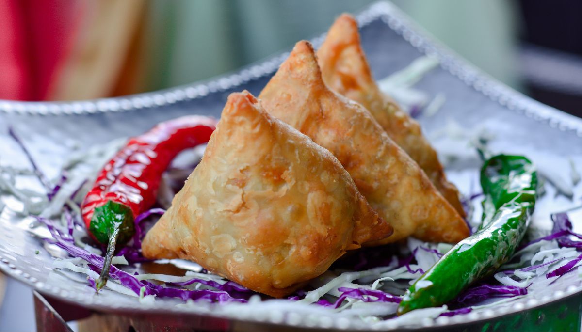 Crispy samosas served with green and red chutney on a plate”