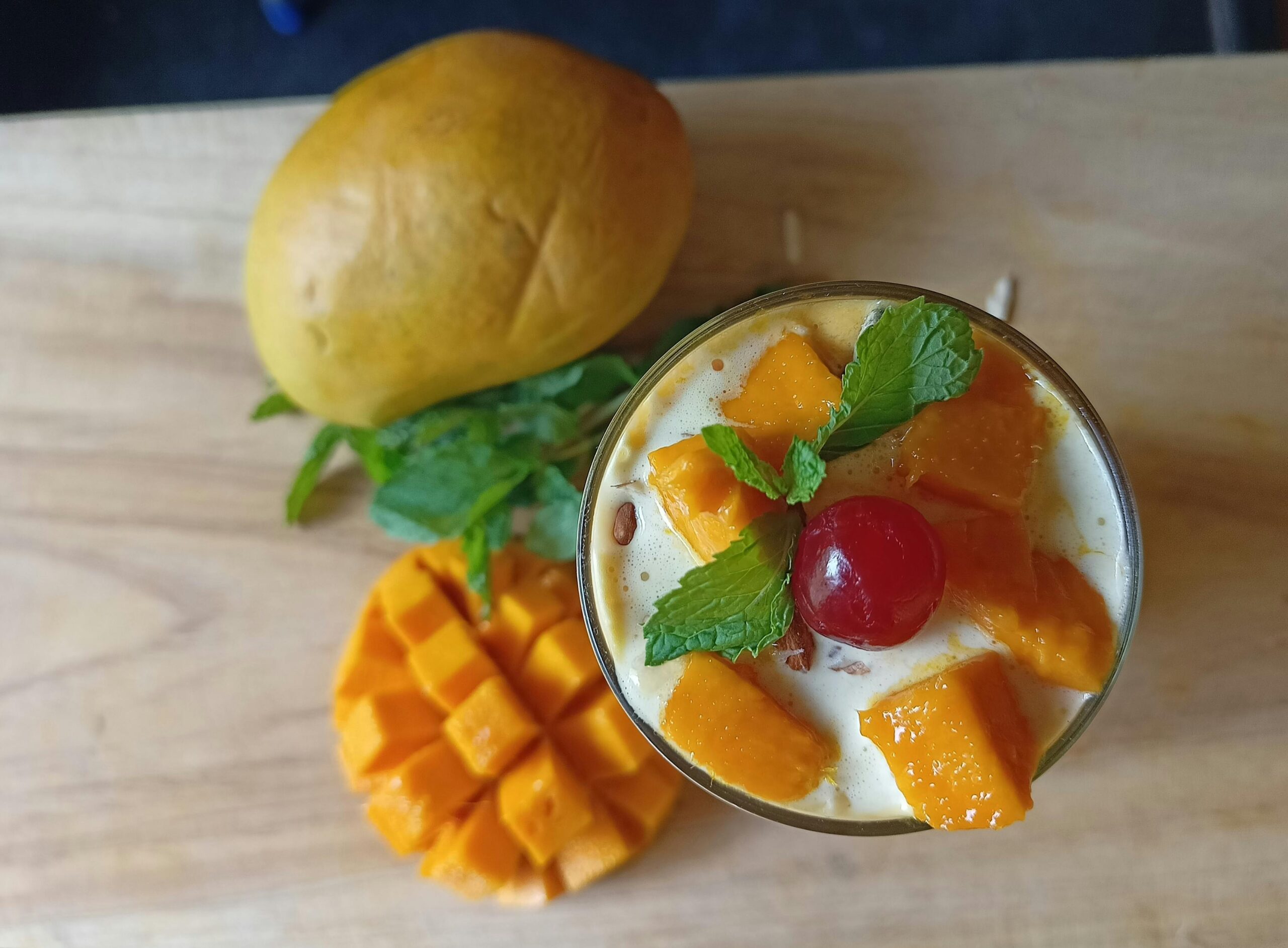 A refreshing glass of healthy mango lassi made with almond milk, topped with fresh mango chunks, a cherry, and mint leaves.