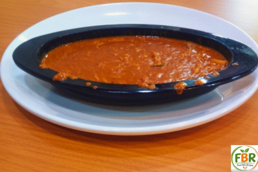 Side view of a creamy Butter Chicken Curry served in a stylish black oval bowl on a white plate.