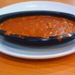 Side view of a creamy Butter Chicken Curry served in a stylish black oval bowl on a white plate.