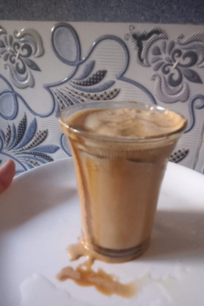 Homemade mocha iced coffee in a glass with frothy top on table